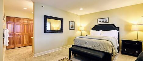 A bedroom with a bed, bedside tables, a bench, a mirror, and a door to a bathroom.
