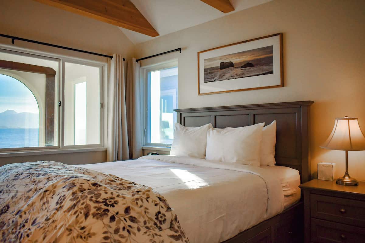 A neatly made bed with a floral bedspread, a framed picture above the bed, and a nightstand with a lamp.