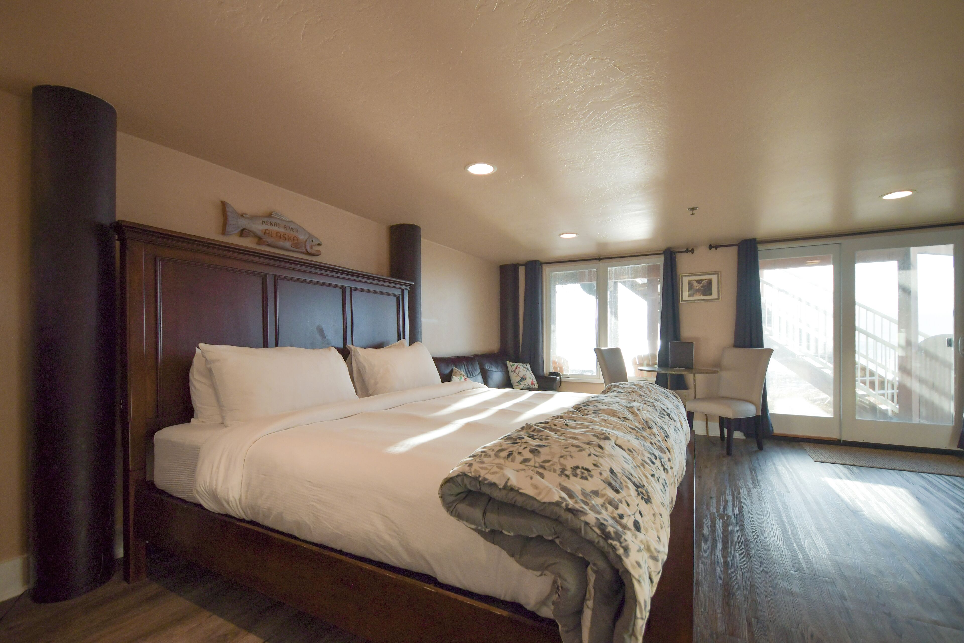 A spacious bedroom with a large bed, a nightstand, a chair, and a view of the outside through a sliding glass door.