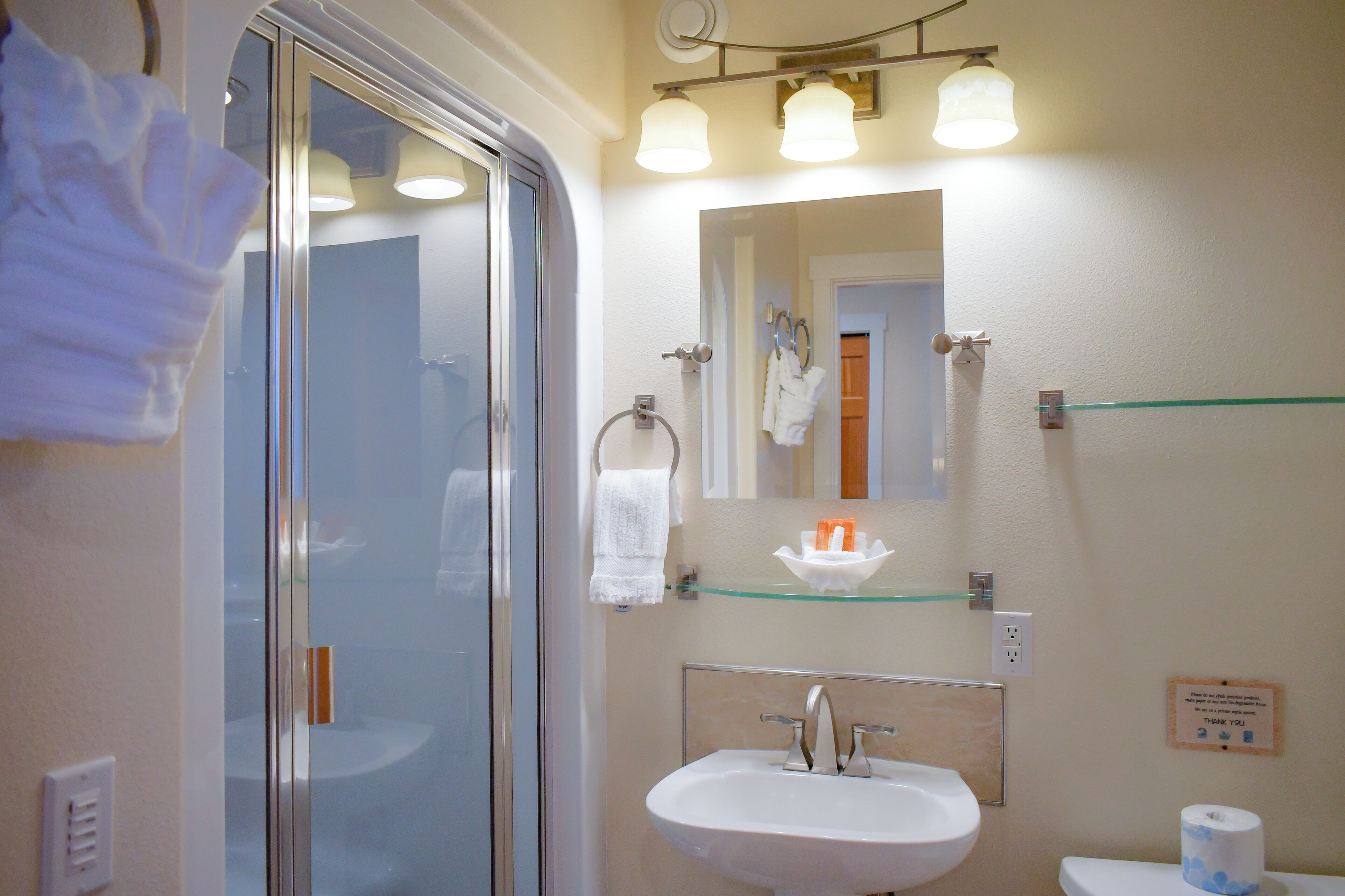 A bathroom with a glass shower door, a sink, a toilet, and a mirror.