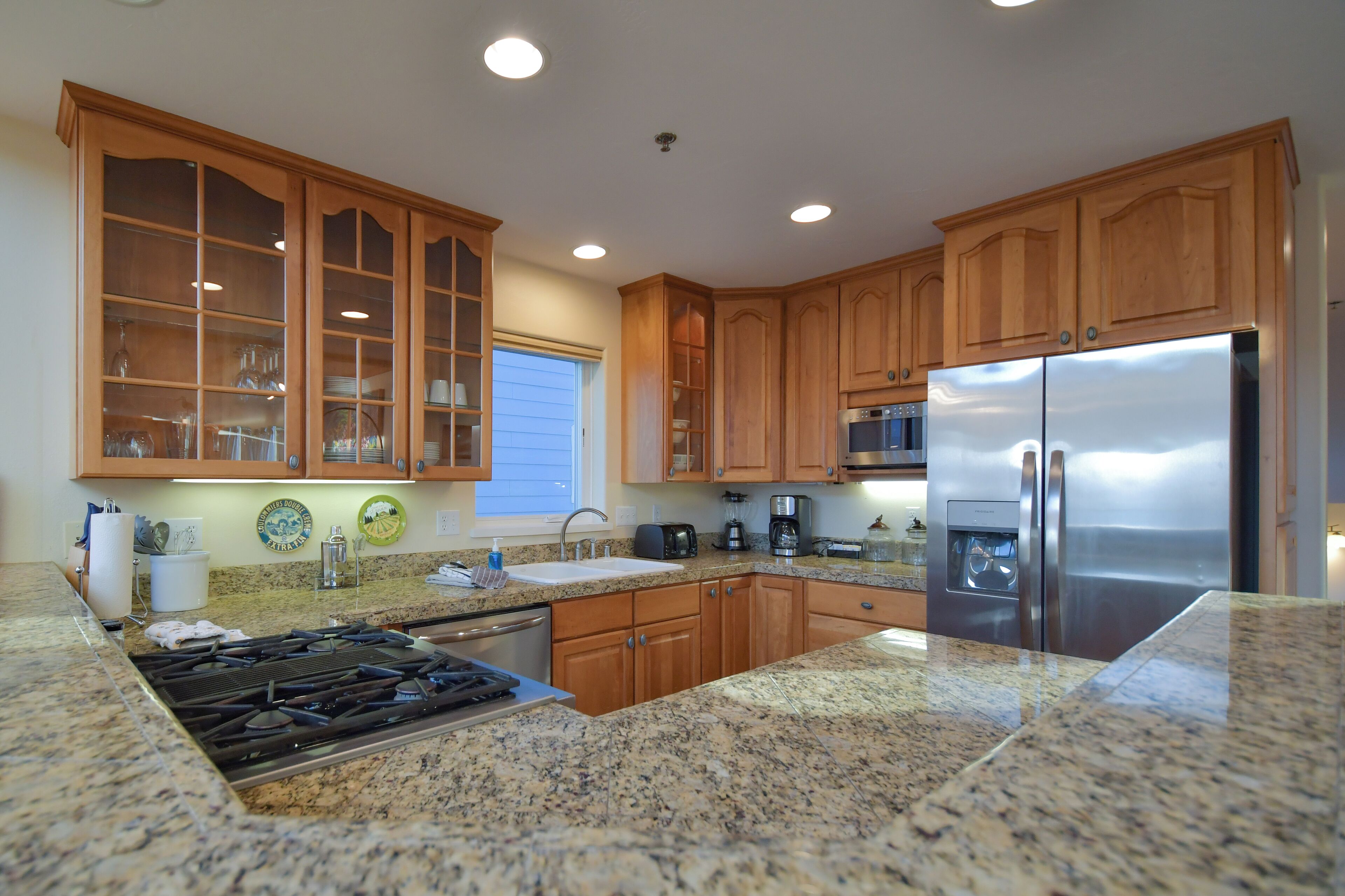 A kitchen with wooden cabinets, granite countertops, a stainless steel refrigerator, and a built-in stove.