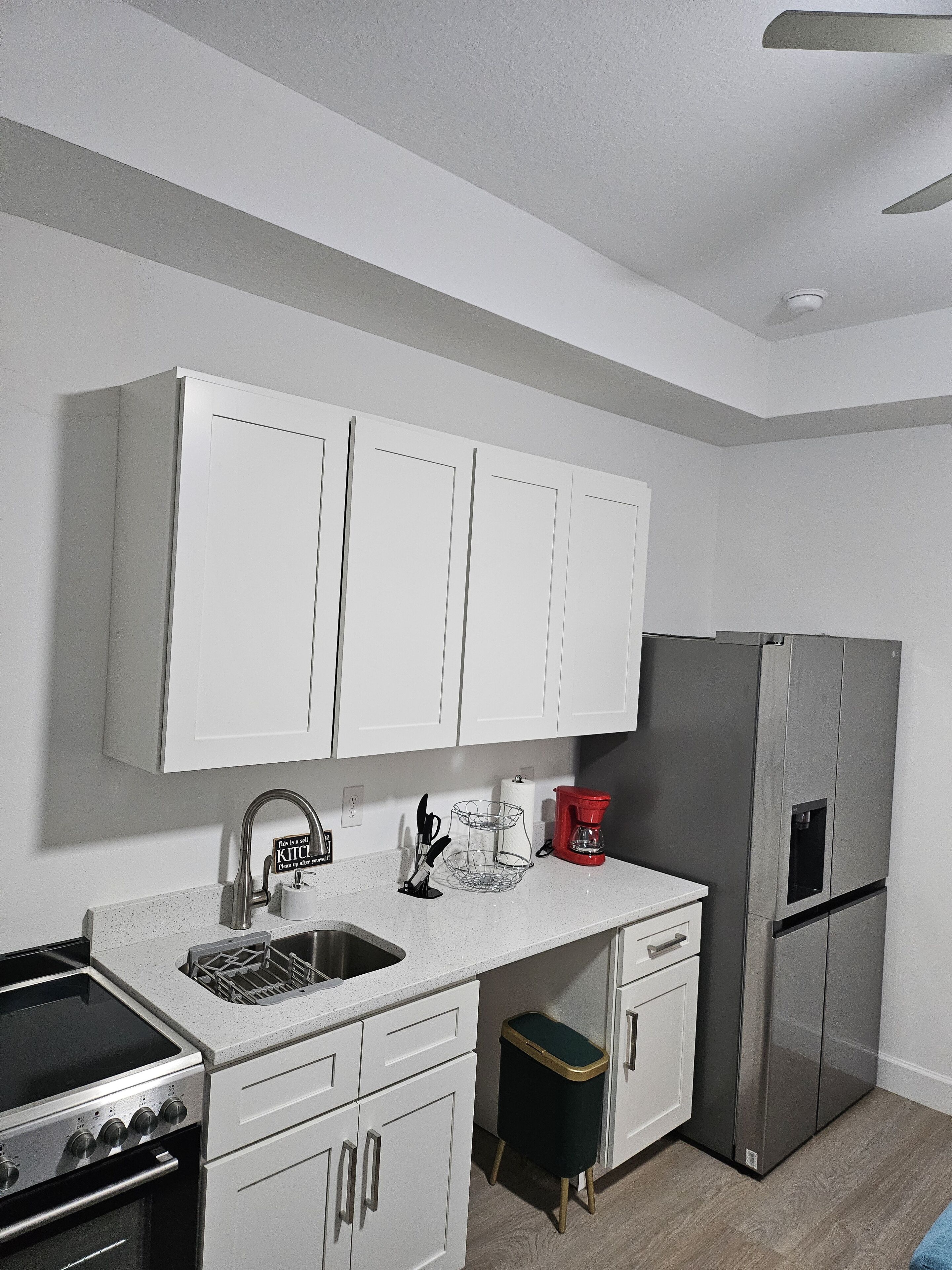 A modern kitchen with white cabinets, a stainless steel refrigerator, a gas stove, and a coffee maker.