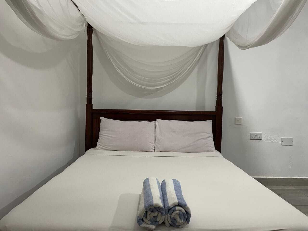 Una cama con dosel, ropa de cama blanca y toallas enrolladas sobre la cama.