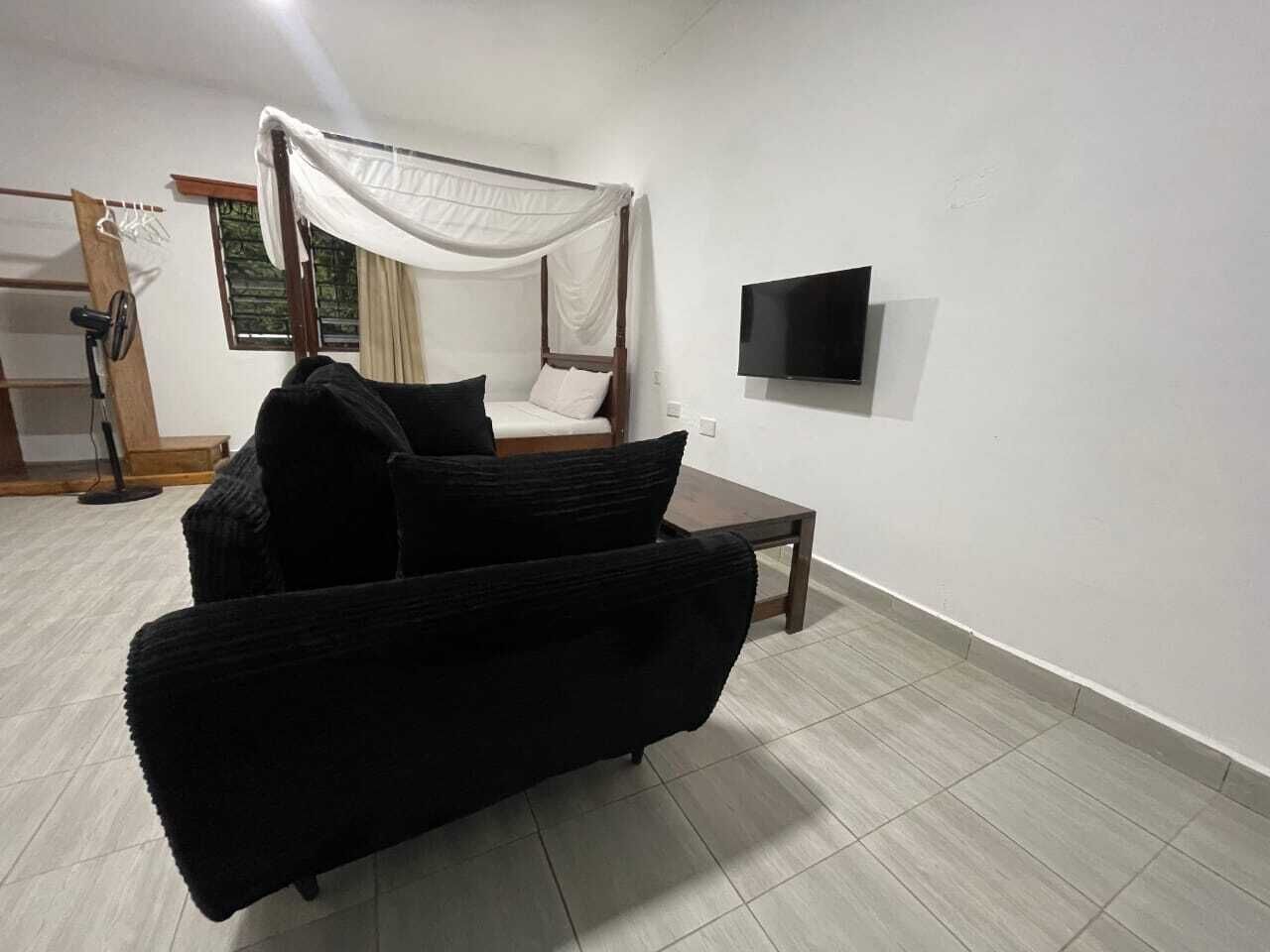 Un dormitorio con una cama, un sofá negro, una mesita y un televisor.