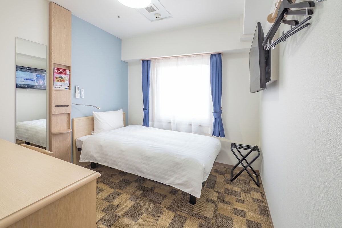 A hotel room with a bed, a desk, a mirror, a television, and a window with curtains.