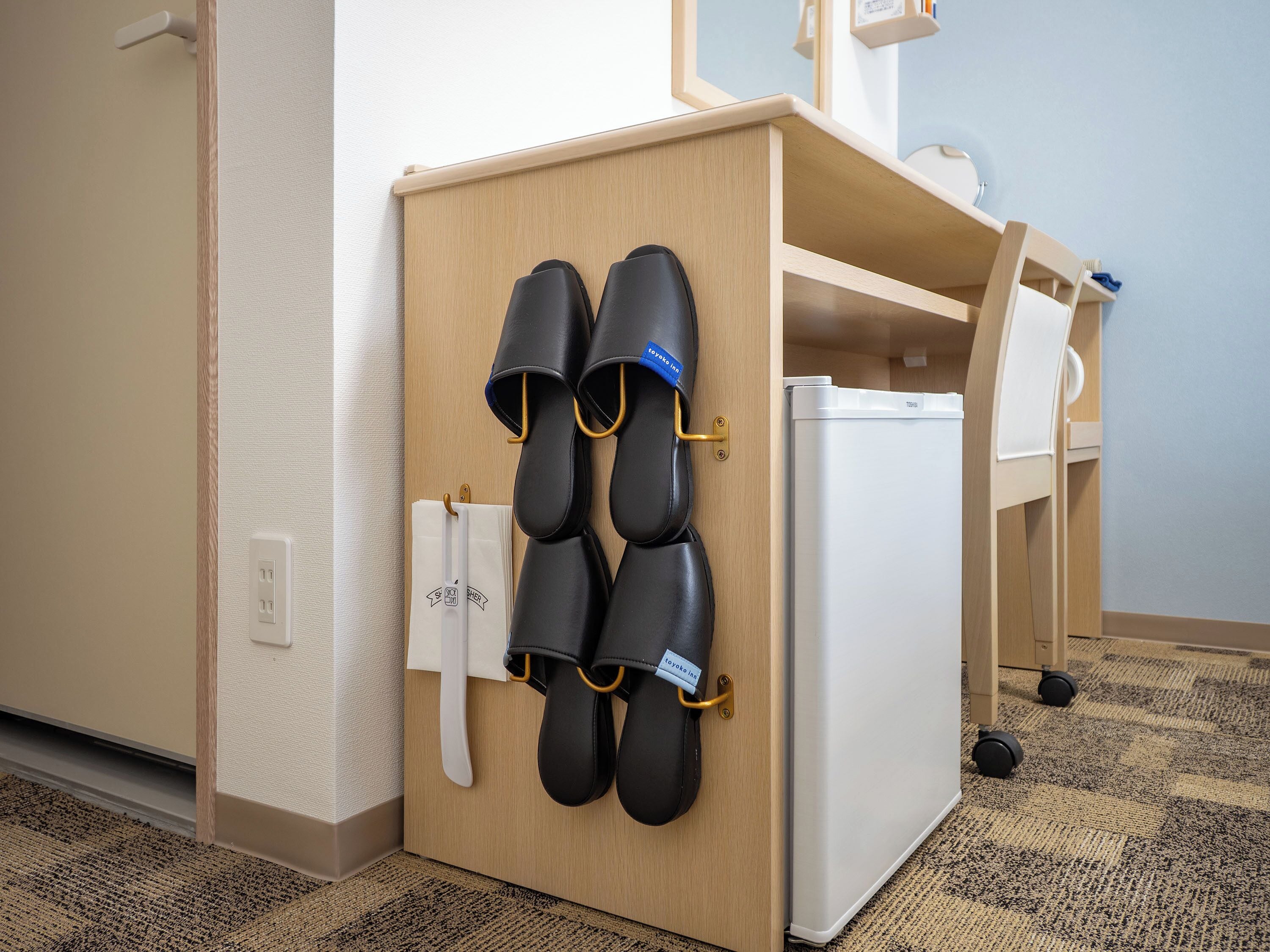 A hotel room with a wooden cabinet holding slippers and a white refrigerator.