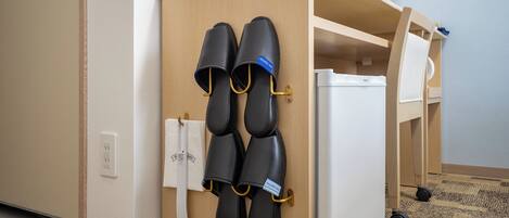 A hotel room with a wooden cabinet holding slippers and a white refrigerator.