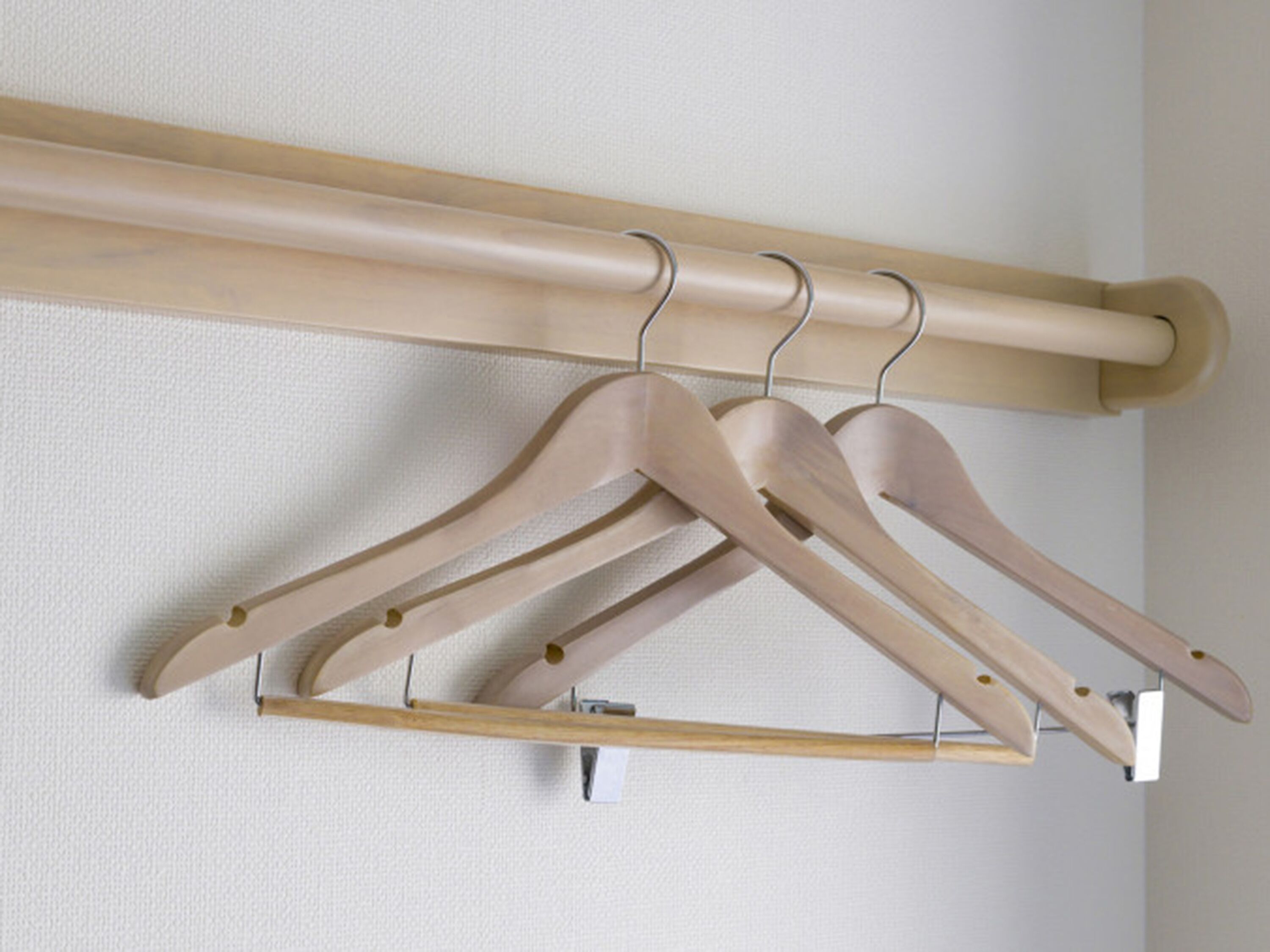 A wooden coat rack with three hangers against a textured wall.