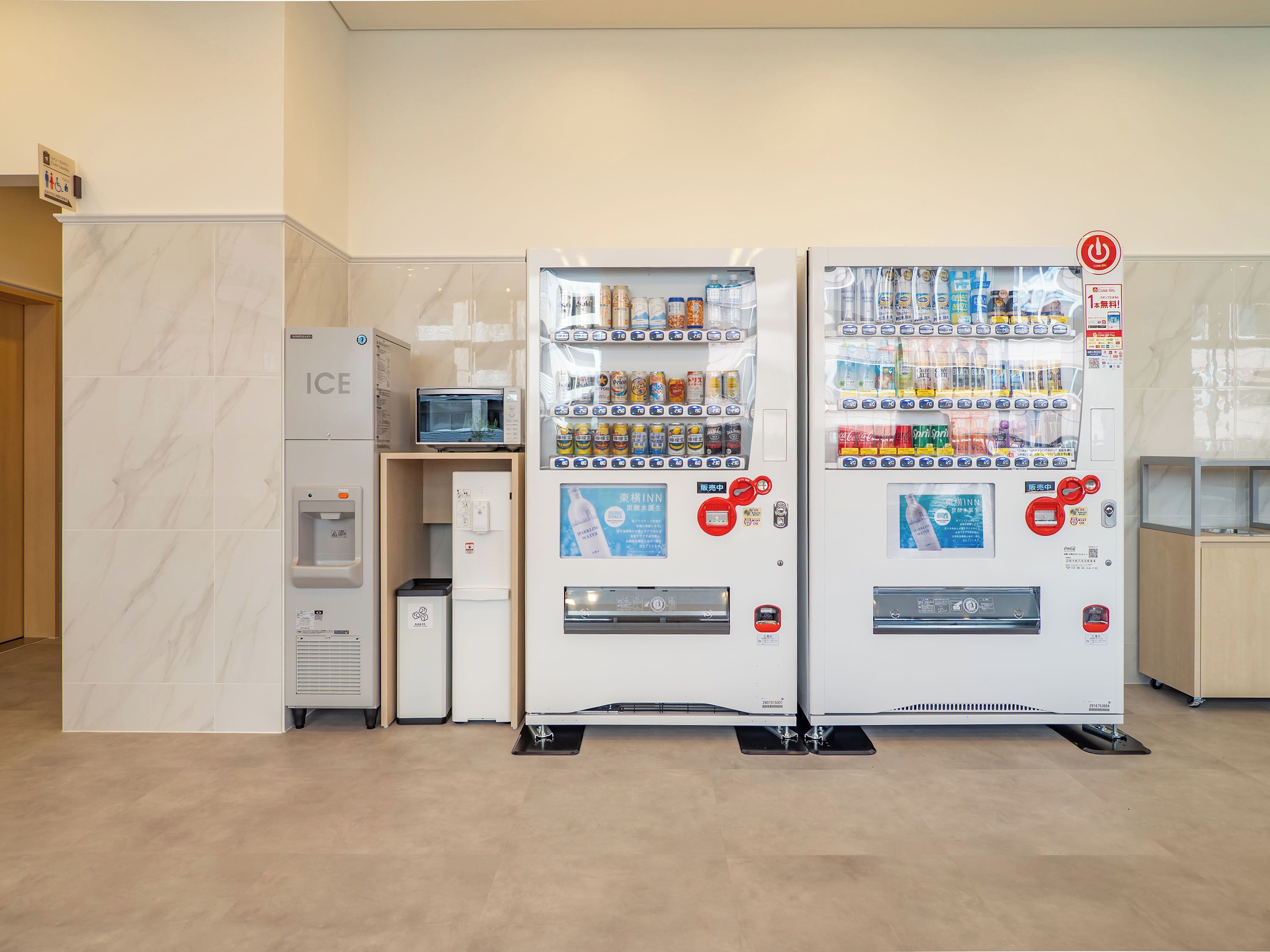 Twee automaten met diverse dranken en snacks, een waterkraan en een magnetron.