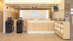 A hotel reception area with a reception desk, two computer stations, a wall-mounted TV, and a shelf with towels. - Toyoko Inn Kobe Sannomiya Ekimae (Kobe)