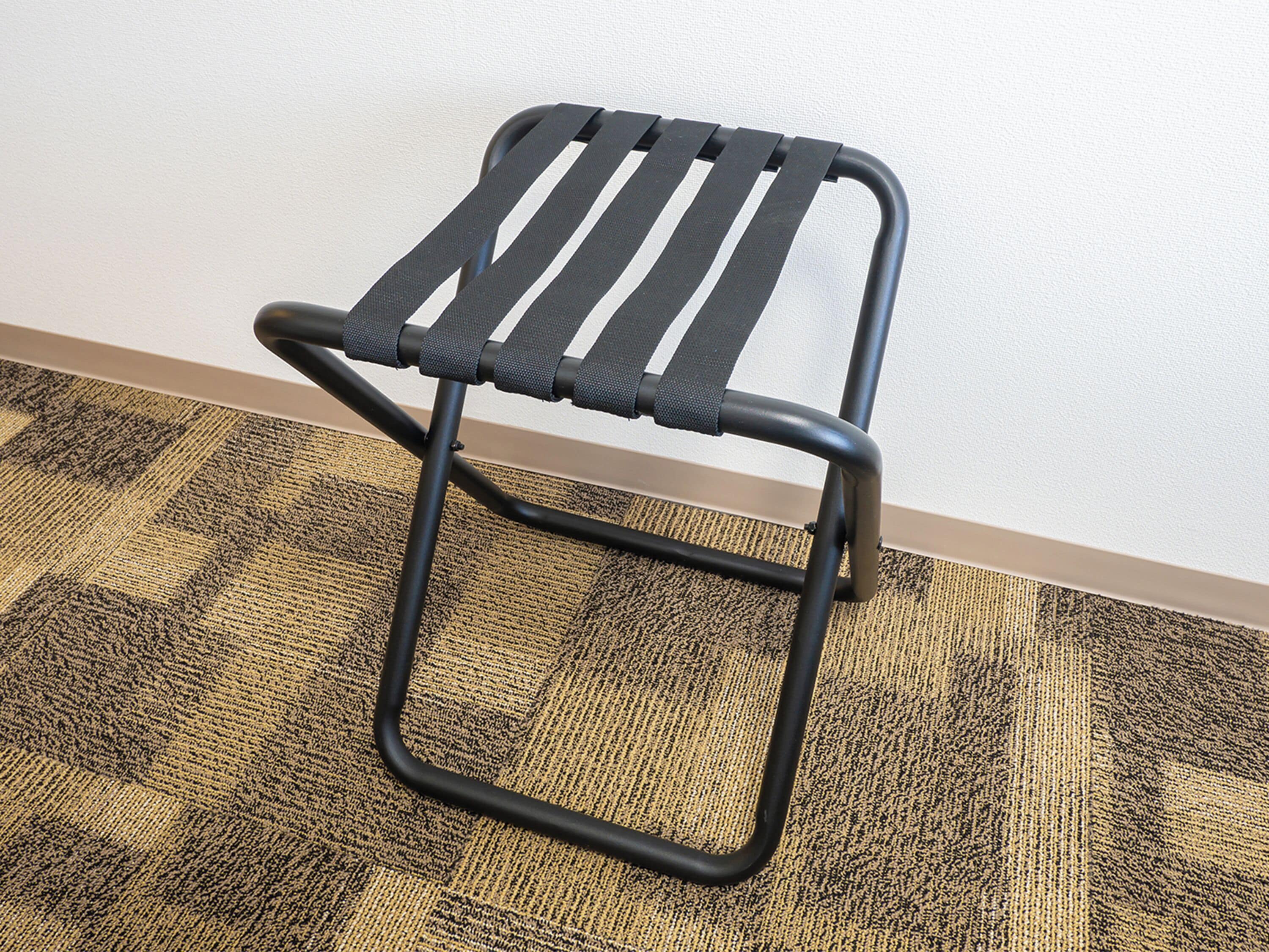 A black metal chair with a woven seat and backrest, placed on a patterned carpet against a plain wall.