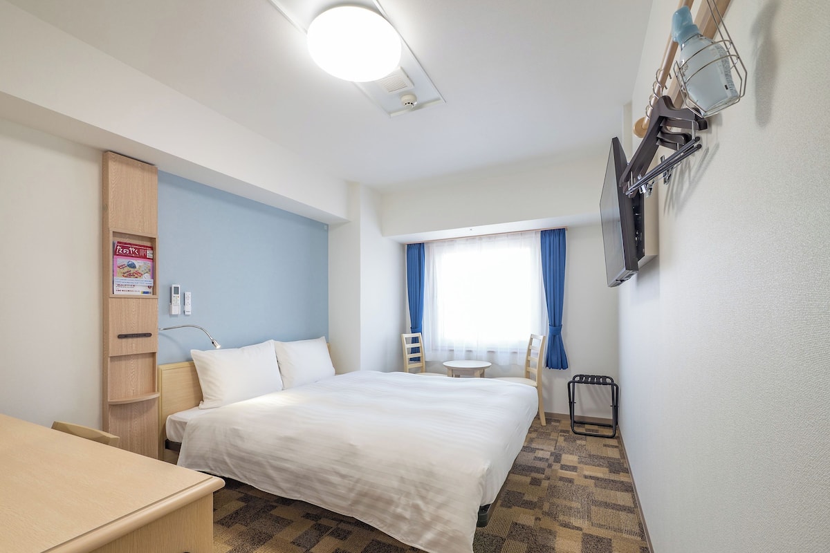 A hotel room with a bed, bedside table, chair, desk, and a small table with a chair.