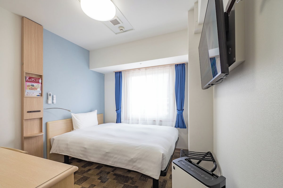 A hotel room with a bed, a desk, a TV, a wardrobe, and a window with curtains.