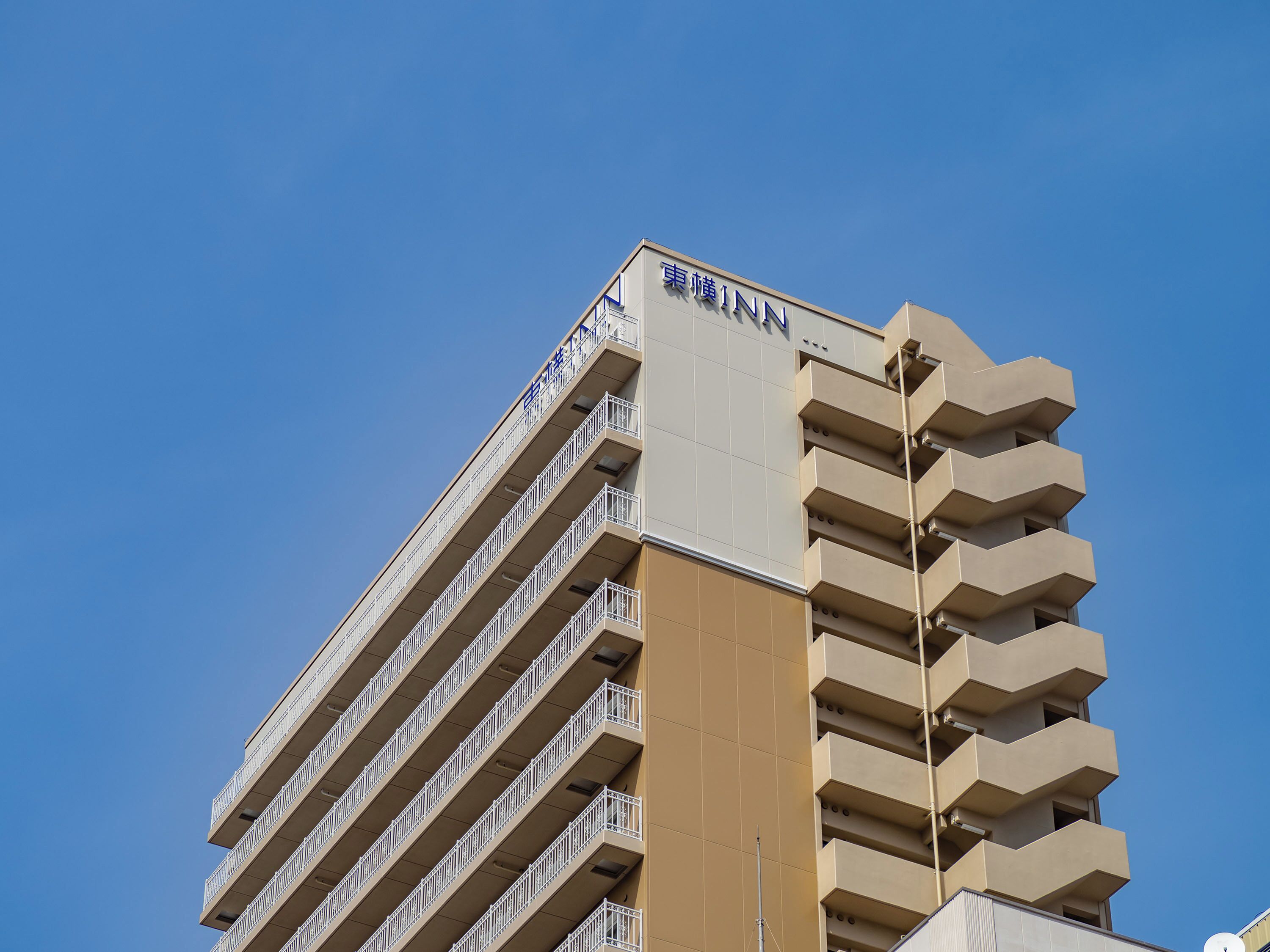 A tall hotel building with multiple balconies and a clear blue sky.