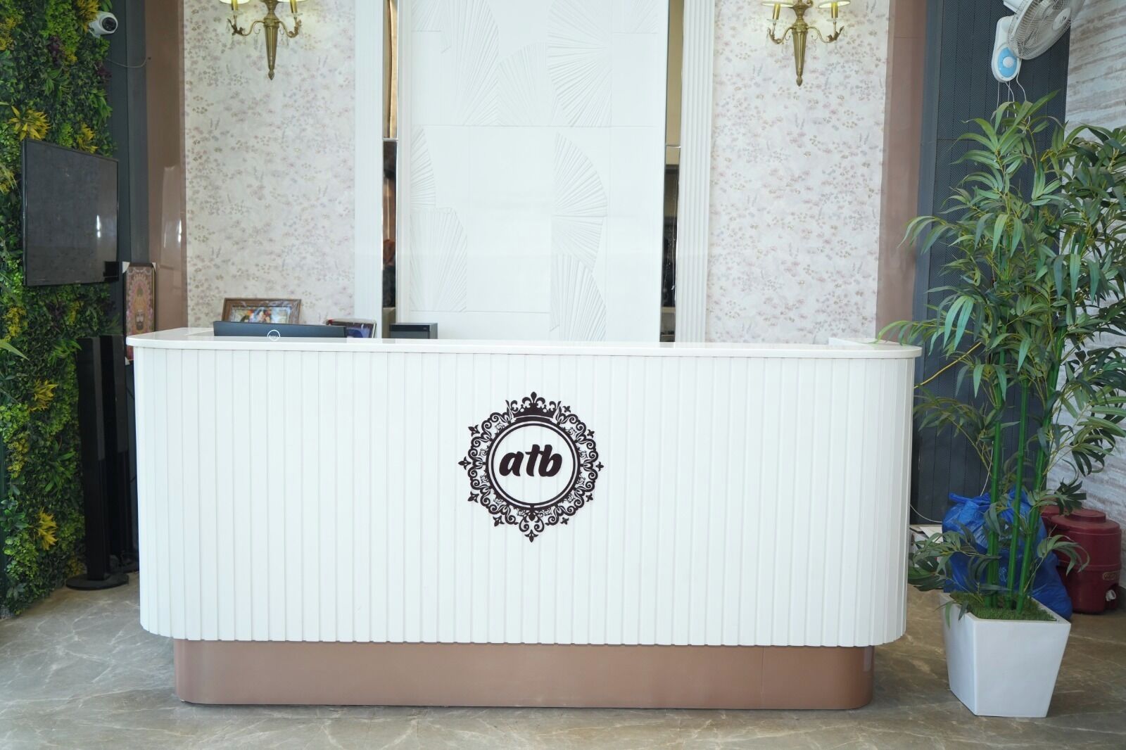 Un comptoir d’accueil avec un logo, un ventilateur fixé au mur et une plante en pot.