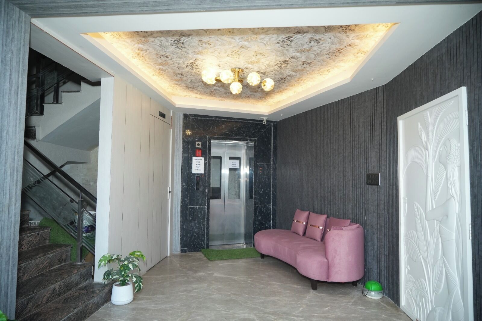 A modern lobby with a curved pink sofa, a staircase, a ceiling light fixture, and a door with a decorative panel.