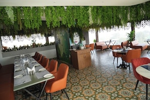 Un restaurant avec une longue table à manger, des chaises orange et des plantes suspendues.
