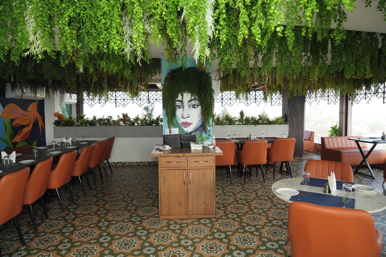 Ein Restaurant mit hängenden Pflanzen an der Decke, Wandmalerei und gemustertem Boden.