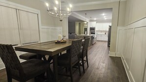 Een eethoek met een houten tafel en stoelen, een kroonluchter en uitzicht op de keuken.