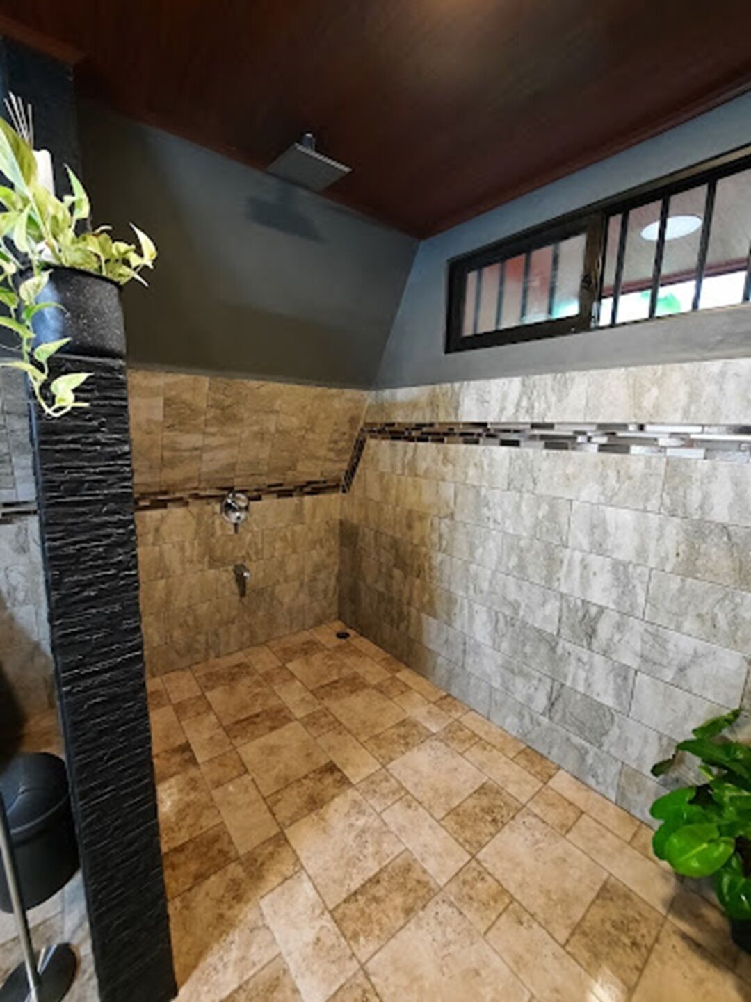 A shower area with stone tiles, a black column, and a window with bars.