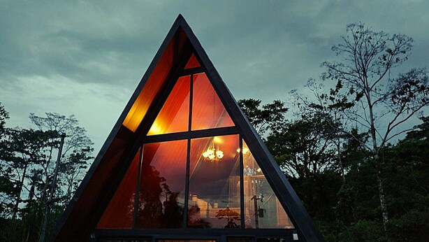 Uma estrutura de vidro triangular com interior visível, rodeada por árvores.