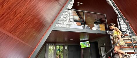 Um interior acolhedor com telhado inclinado, um sofá, uma escada e uma televisão.