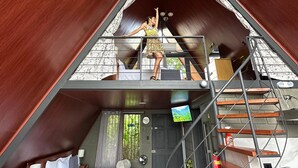 Quarto estilo loft com teto inclinado, uma cama, um sofá e uma escada.