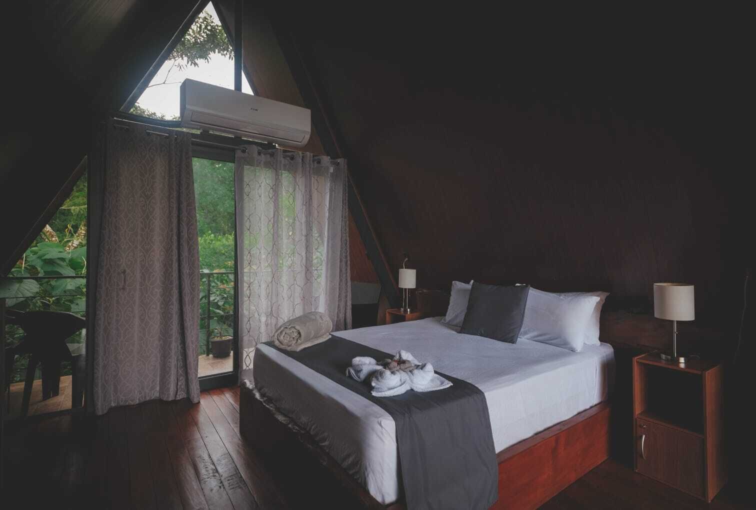 Un dormitorio con una cama grande, dos mesitas de noche con lámparas, una ventana con cortinas y vistas al exterior.