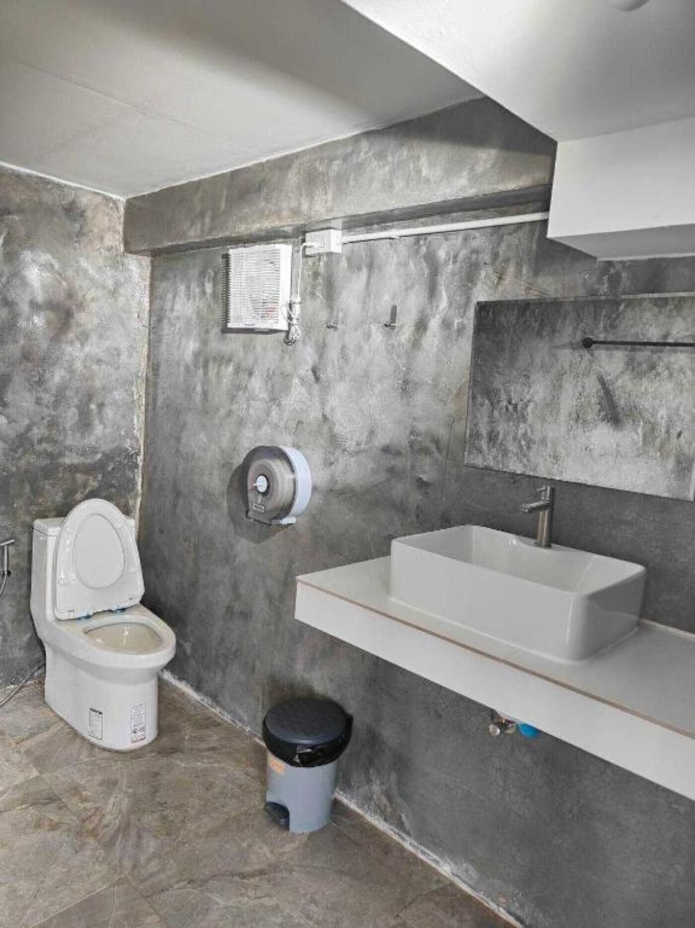 A bathroom with a toilet, a sink, a trash bin, and a towel rack.