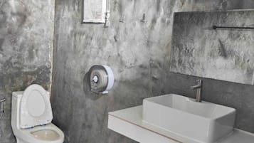 A bathroom with a toilet, a sink, a trash bin, and a towel rack.