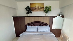 Ein Hotelzimmer mit einem Bett, einem Gemälde darüber und je einer Zimmerpflanze auf beiden Seiten.
