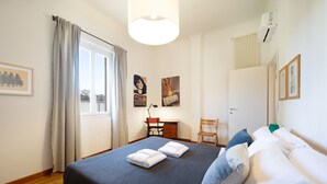 Un dormitorio con una cama, dos sillas, un escritorio y una ventana con cortinas.