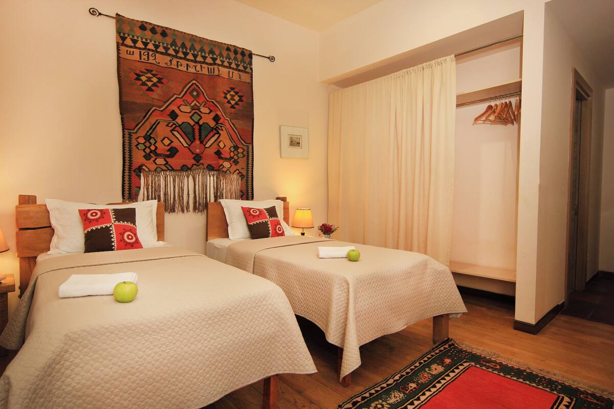 A hotel room with two beds, a large tapestry, a wardrobe, and a red rug.