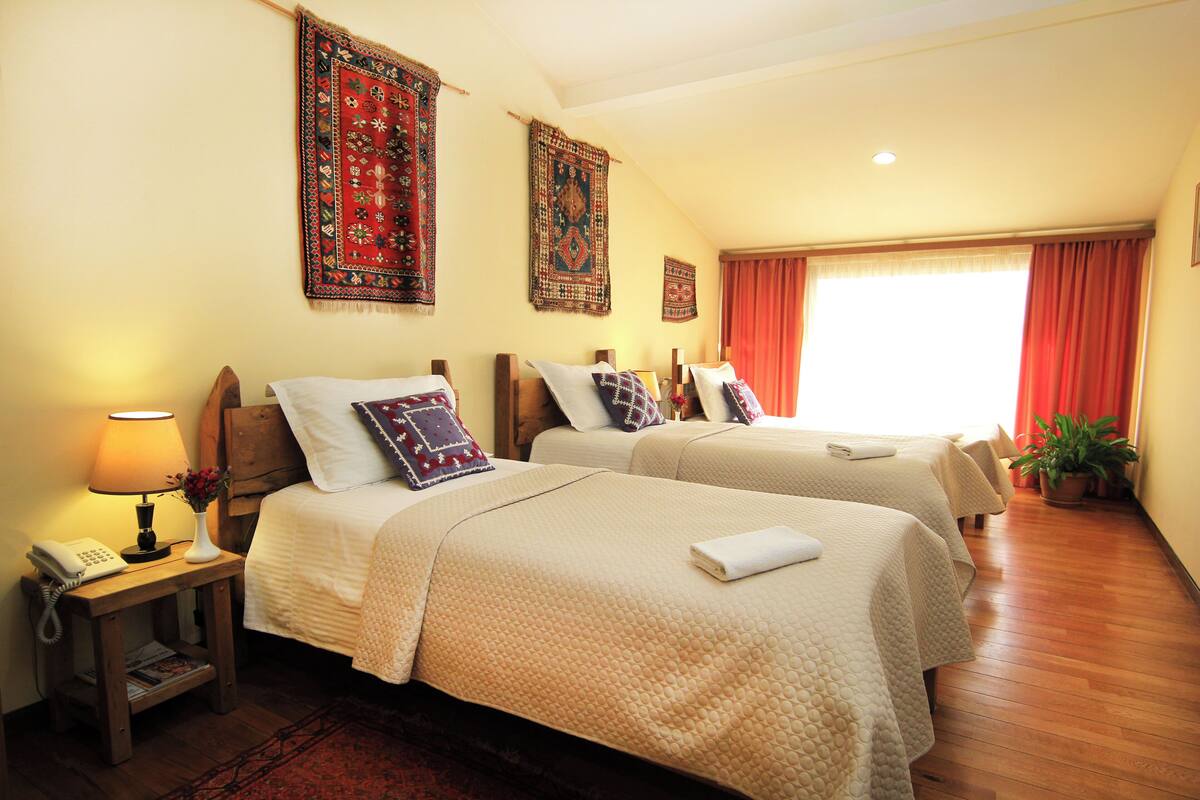 A hotel room with two beds, a nightstand with a lamp, a telephone, and a window with curtains.