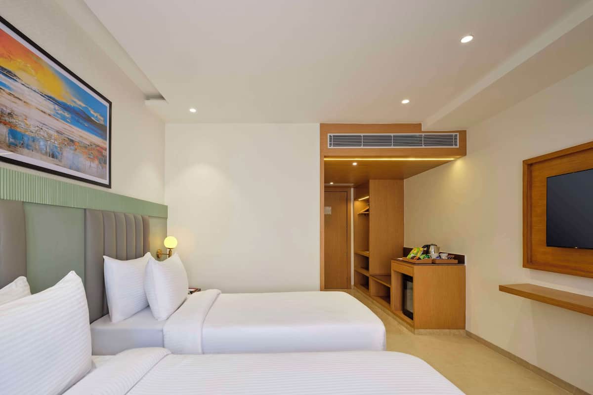 A hotel room with two beds, a painting, a desk with a coffee maker, and a TV mounted on the wall.