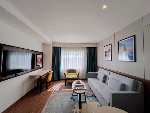 A modern hotel room with a flat-screen TV, a sofa, a chair, a small table, and a large window with curtains. - Tulip Inn Bhopal (Bhopal)