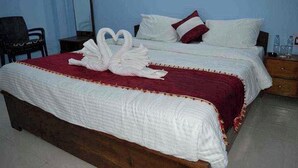 A double bed with white bedding and a red accent, a wooden nightstand with a mirror, and a chair in a room with light blue walls. - Hotel Yumi Ragi (Papumpare)