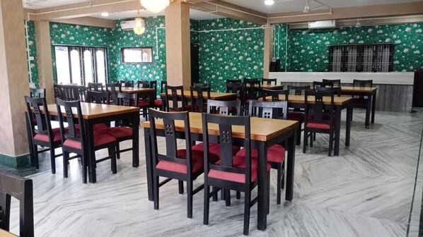 Een restaurant met meerdere tafels en stoelen, een toonbank en een behang met patroon.