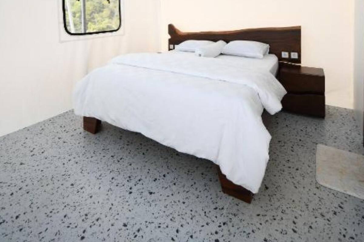 A bedroom with a bed, a wooden headboard, a nightstand, a ceiling fan, and a window with a view of greenery.