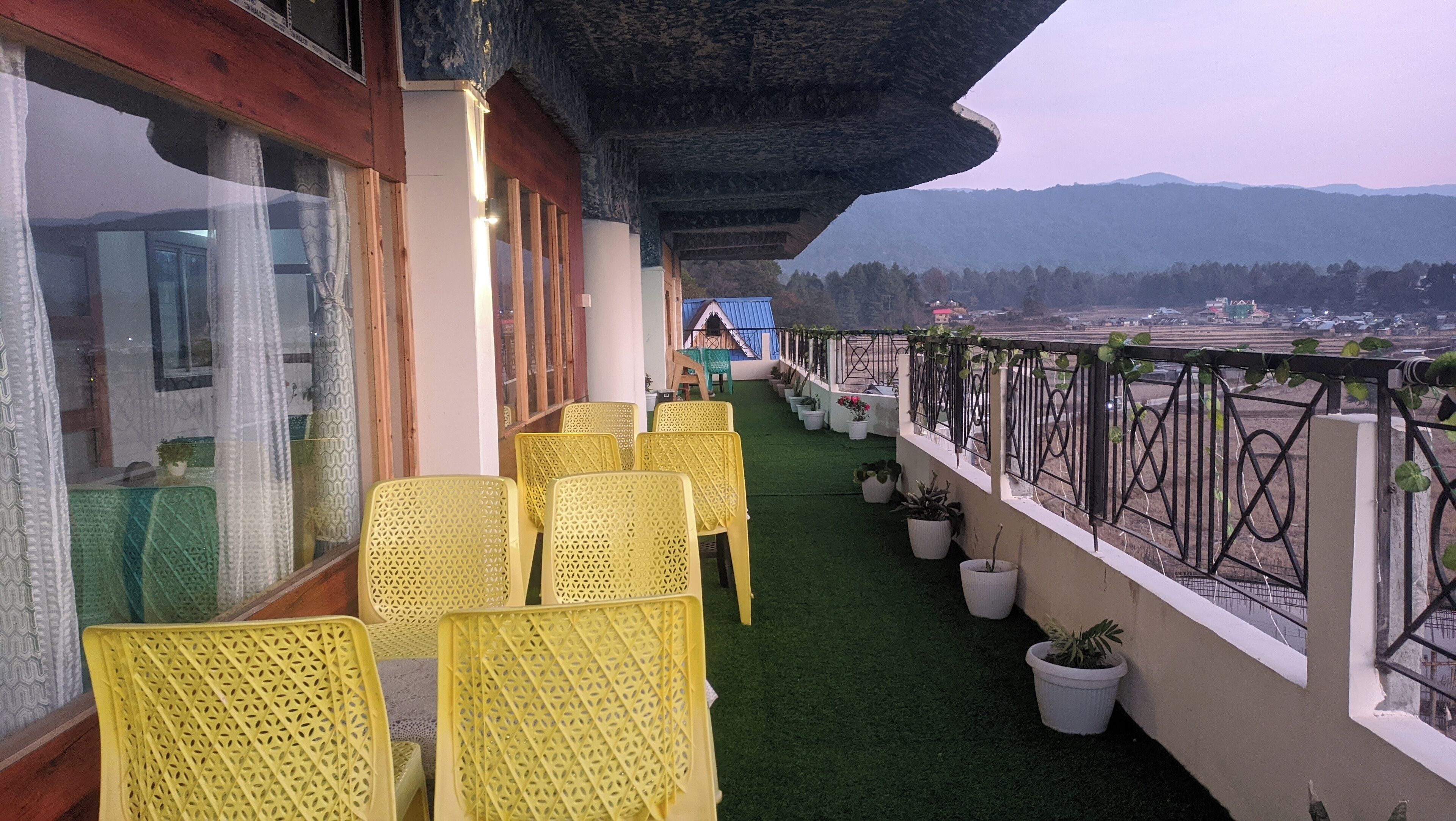 A balcony with yellow chairs, potted plants, and a view of distant mountains.