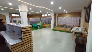Un interno moderno con una reception, elementi in legno, un'area salotto con tavoli e sedie, e una vista attraverso ampie finestre.