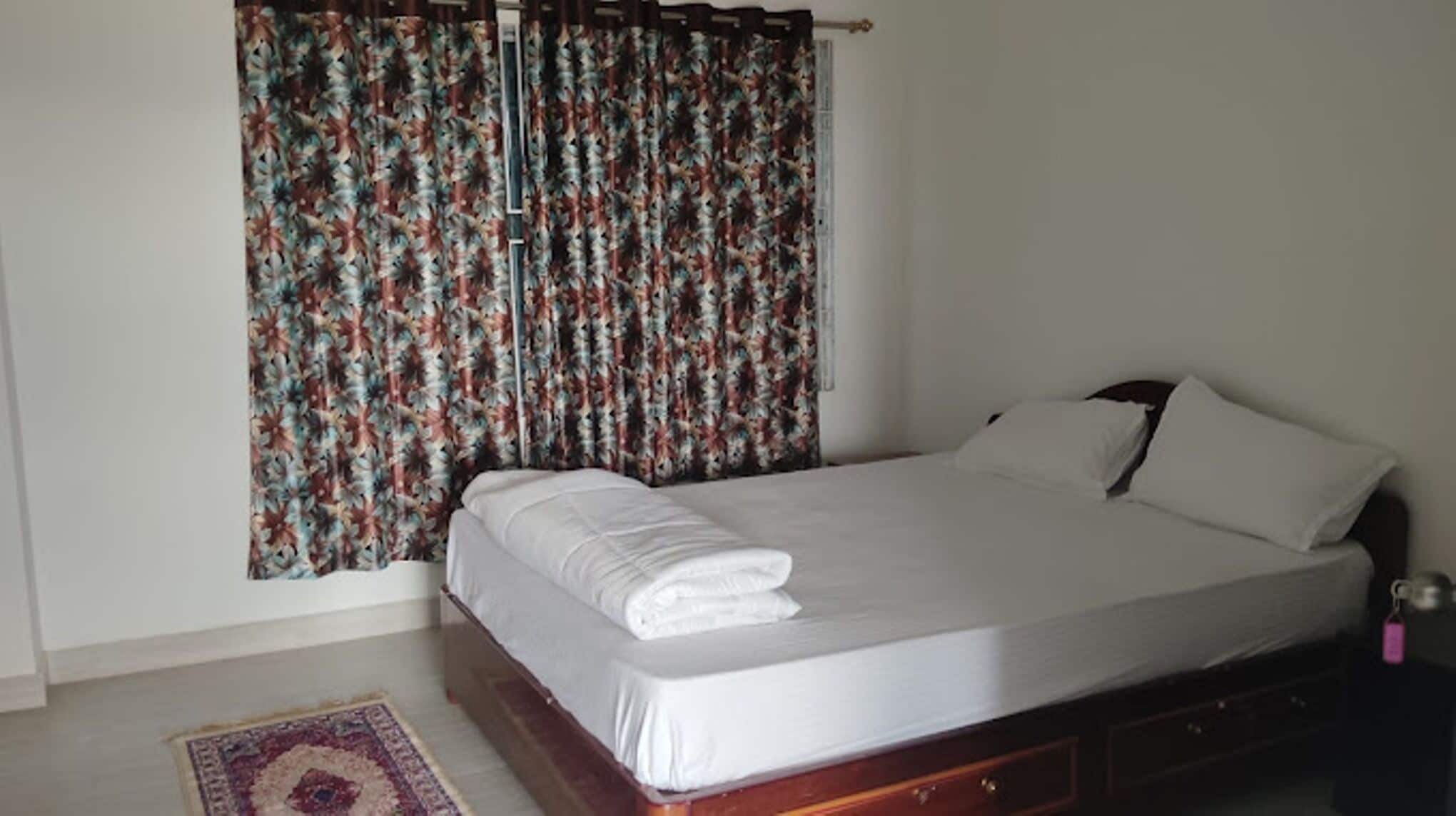 A neatly made bed with white linens, a wooden headboard, and a floral curtain.