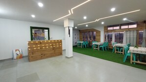 Un'area reception con un bancone in legno, erba sintetica verde e tavoli con sedie.