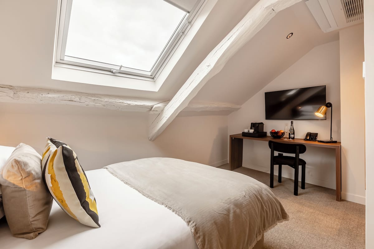Ein Schlafzimmer mit Dachfenster, einem Bett mit Kissen, einem Schreibtisch mit Stuhl und einem Flachbildfernseher.