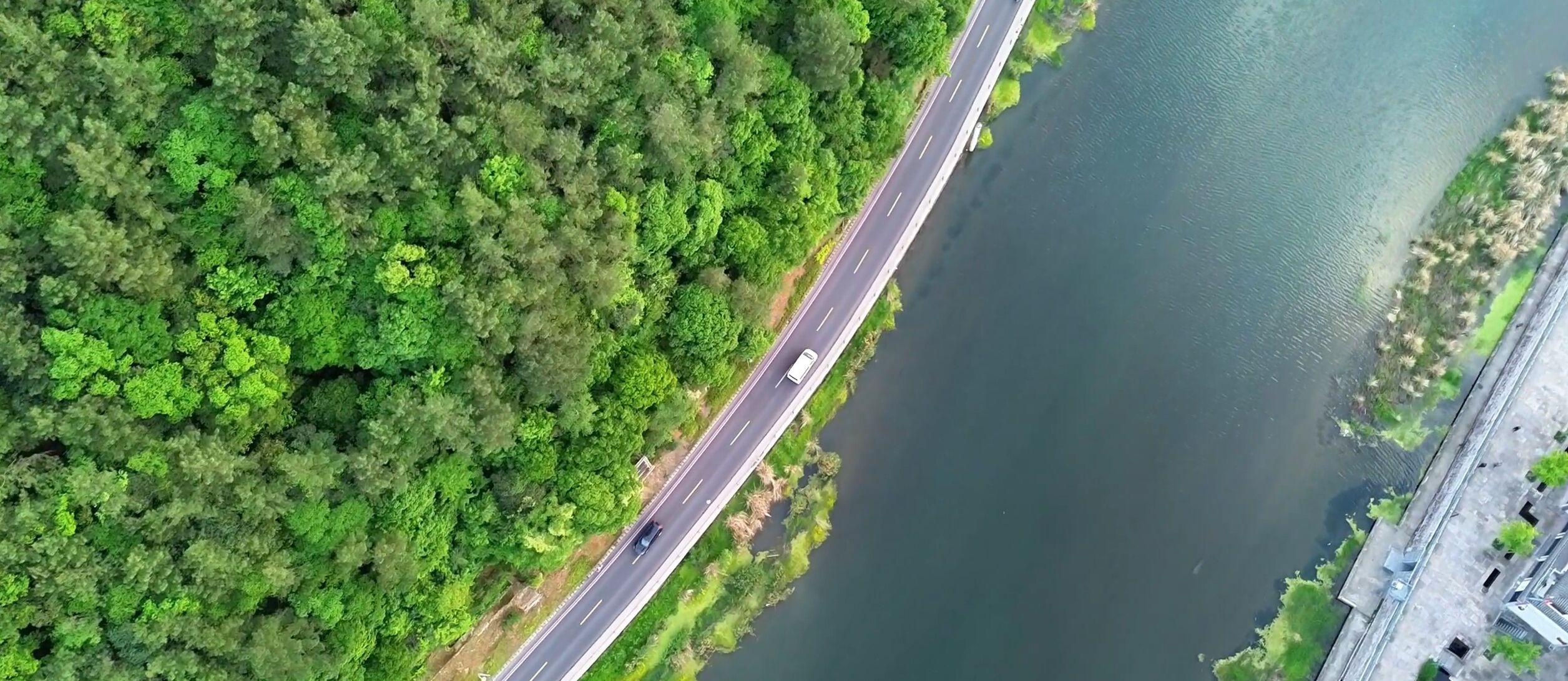 An aerial view of a bridge over a river with dense greenery on both sides.