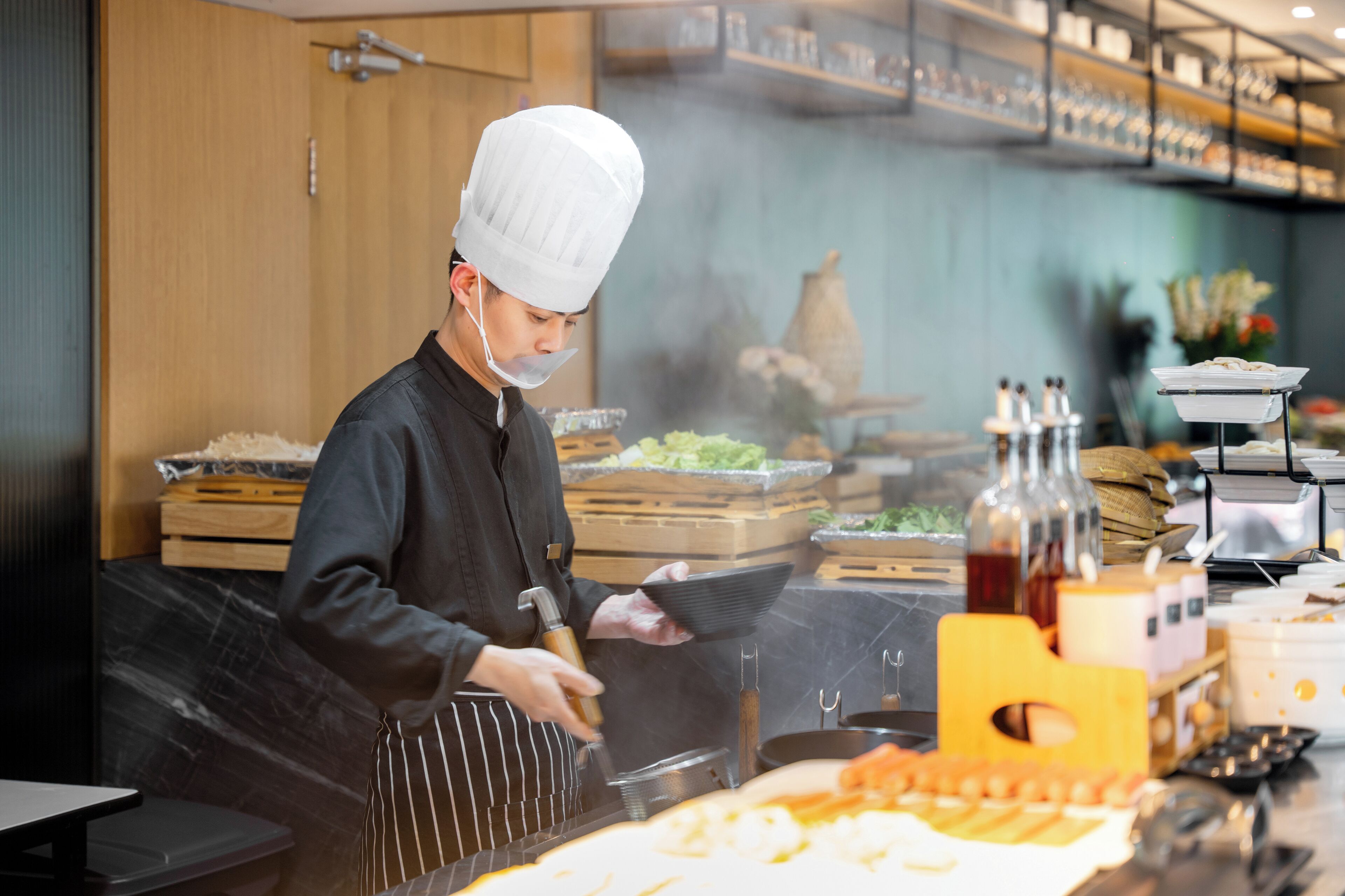 Un chef en una cocina profesional, centrado en la preparación de alimentos, incluyendo una parrilla y diversos utensilios de cocina.