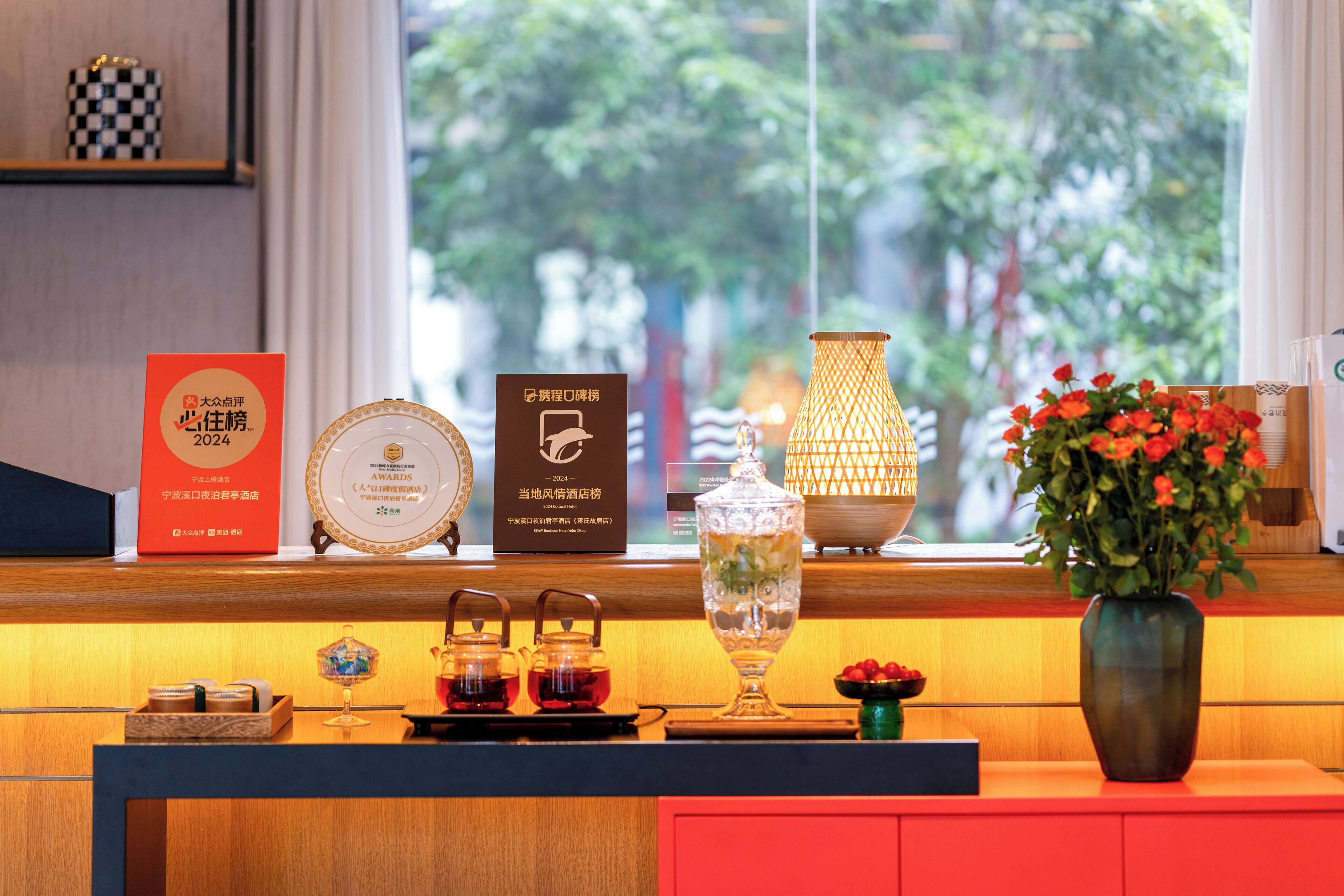 A hotel reception desk with a window view, a vase of flowers, and various decorative items.