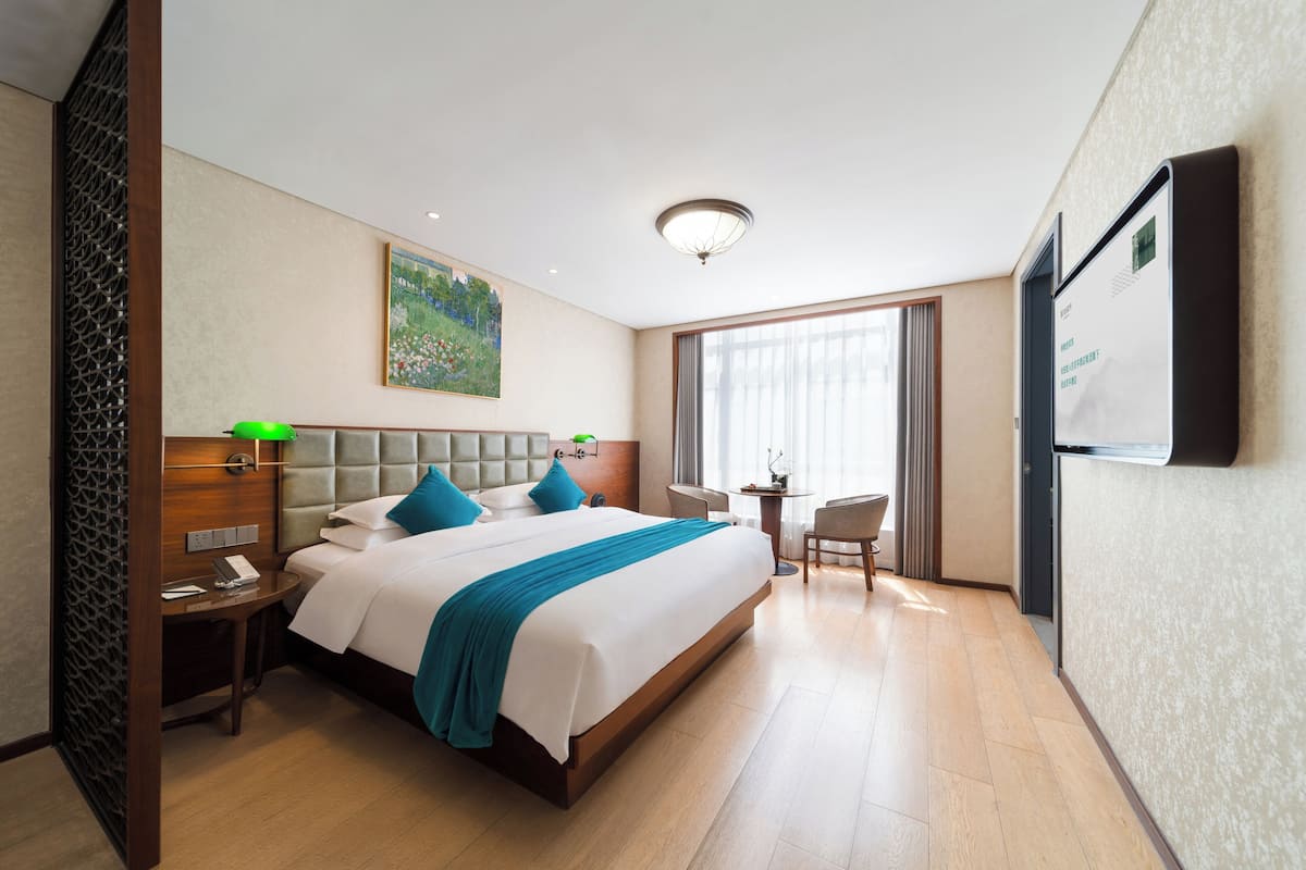 Une chambre d’hôtel avec un grand lit, un bureau, une chaise, une petite table, un téléviseur et une fenêtre avec des rideaux.