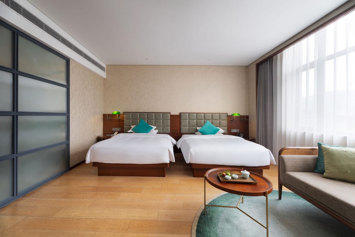 Une chambre d’hôtel avec deux lits, un canapé, une petite table et de grandes fenêtres.