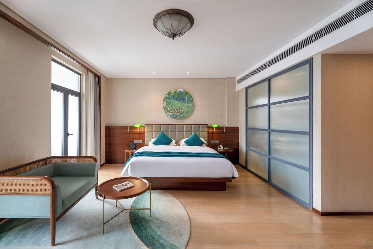 Une chambre d’hôtel moderne avec un grand lit, un canapé, une petite table et une grande fenêtre.
